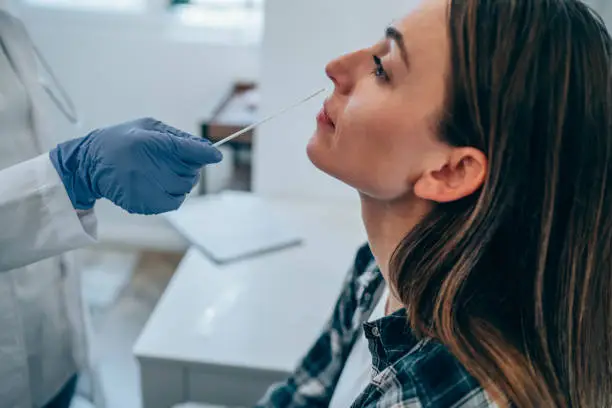 Shot of a doctor using cotton swab while doing coronavirus PCR test at the hospital. Doctor laboratory assistant takes swab from nose of sick patient. Unrecognizable doctor with protective glove taking coronavirus sample from female patient's nose.