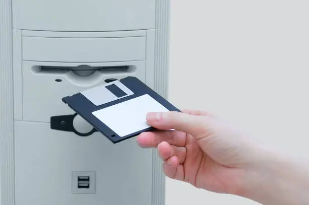 A hand inserts a floppy disk into a personal computer. Retro technology.