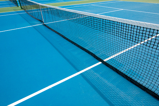 Wide angle view of a blue painted tennis court with net throwing shadows and white lines