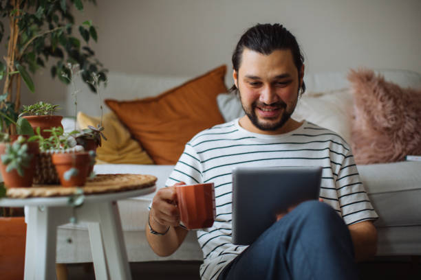 istock Man holding coffee cup and digital tablet while looking away at home 1310651559
