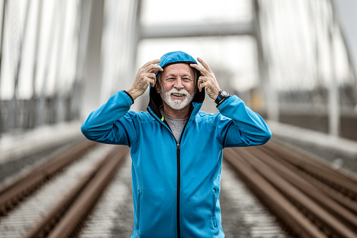 Senior male sportsman looking at camera while on an outdoor pursuit. He is running on a bridge next to train tracks.