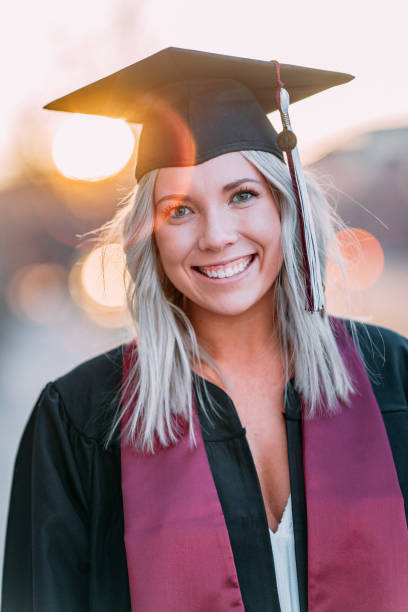 Lens Flare Artistic Close-Up Portrait of a Happy College University Graduate Portrait of a Happy, Confident, Successful College University Graduate Young Woman Wearing a Maroon School Color Sash and a Mortarboard Graduation Cap and Tassel at Sunset Outdoors golden hour wine stock pictures, royalty-free photos & images