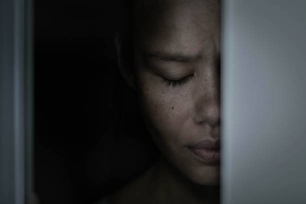 A sad afraid woman hiding in a dark closet alone at home. stock photo