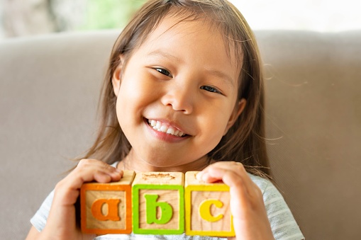 A cute happy little girl holding acb blocks, proud of her self.