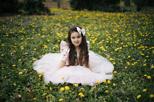 A sweet little three year old girl lays in the grass on a sunny summers evening.  She is dressed casually and smiling as she poses for a portrait.
