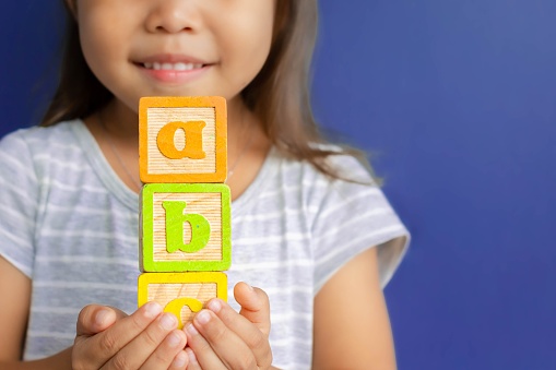 A little girl holding abc blocks infront of a blue background in class.