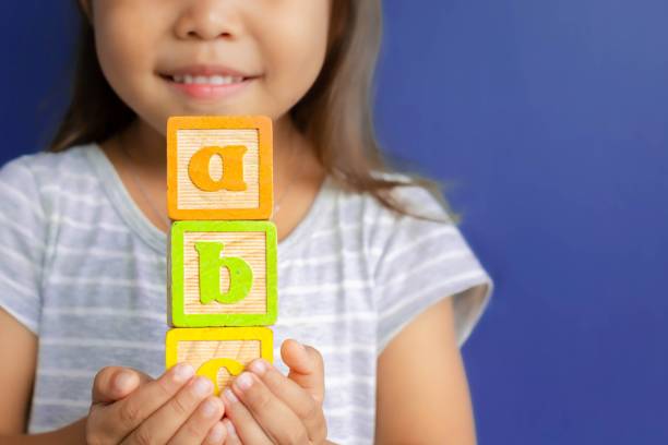 A happy little kid learning abc with blocks. Children learning. A little girl holding abc blocks infront of a blue background in class. alphabetical order photos stock pictures, royalty-free photos & images