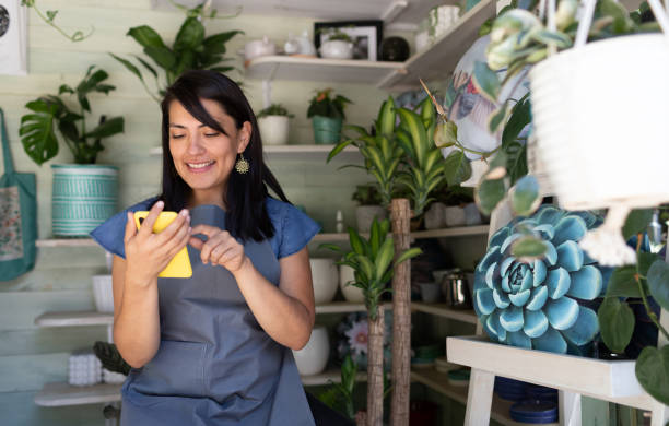 Young woman smiling using mobile phone in her garden shop stock photo
