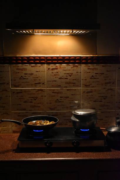 Modern white kitchen with counter and red details, minimalist interior with light in nighttime. Full set of kitchen equipment, pan, pot, electric hob, flipper, vegetable, fruit.