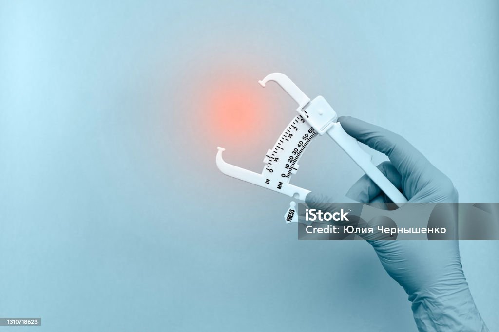 Hand with a device for measuring subcutaneous fat. Caliper for measuring the thickness of subcutaneous fat in the hand, with a rubber glove, in light blue tones. With a red glowing accent at the research site. Overweight Stock Photo