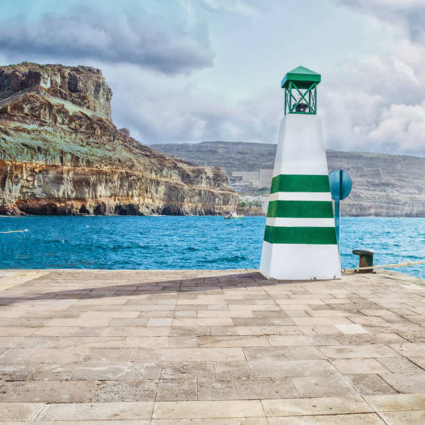 Lighthouse on the pier. Cloudy sky. Mountains. Square orientation. Natural background.