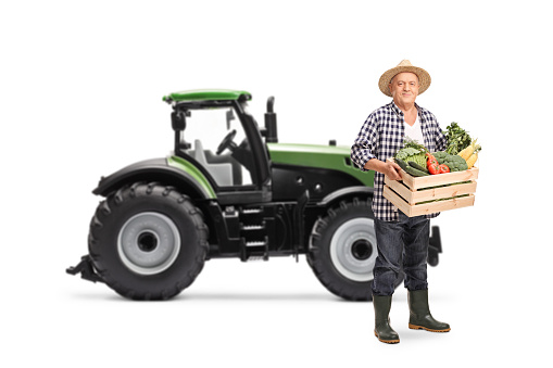 Elderly farmer with a tractor carrying a wooden crate full of vegetables isolated on white background