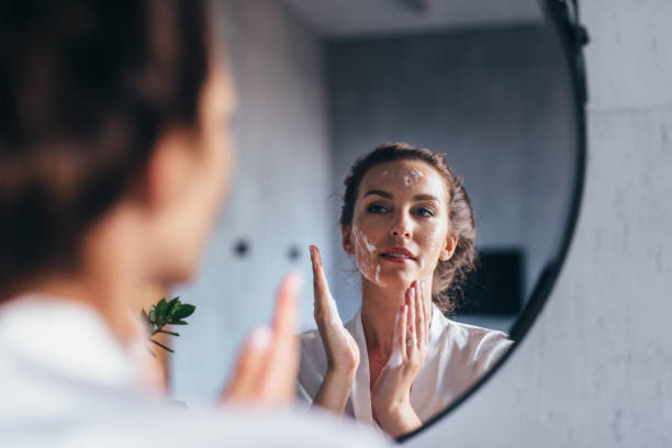 la femme se lave devant le miroir, appliquant la mousse à son visage - exfoliation photos et images de collection