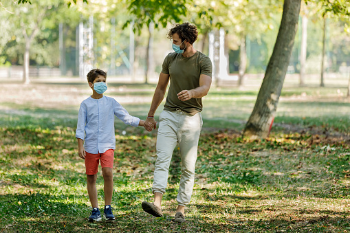 Portrait of Father and Son Walking in the Public Park and Having a Lovely Conversation. A Family With Face Masks is Relaxing in City Park.