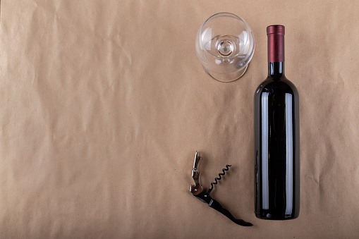 Wine bottle, glass and corkscrew on a brown background. Space for text. Top view.