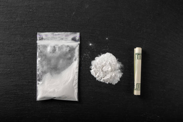 Cocaine in a plastic package on a black background, close-up. A rolled up dollar bill for drug use. Cocaine in a plastic package on a black background, close-up. A rolled up dollar bill for drug use. Prohibited drugs. cocaine stock pictures, royalty-free photos & images