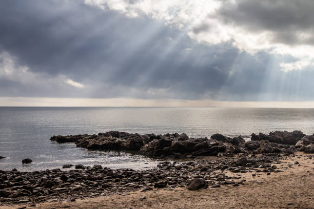 sun's rays over the sea with sand and rock beach