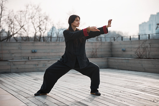 Adult having tai chi workout out on the roof with right leg slightly stretched back and arms moving before body