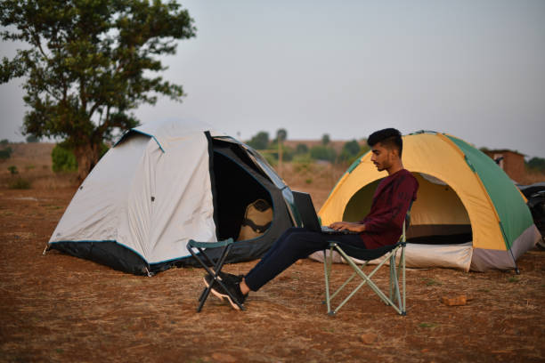 istock Young man working on laptop sitting outdoors near tent 1310729281