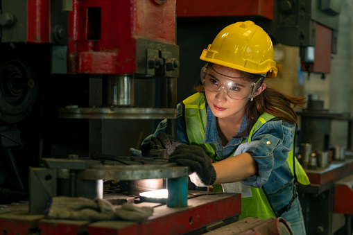 Female worker in hard hat and safety glasses working in the manufacturing industry on business day. Technician engineer control machines in an industrial factory. Workplace gender equality concepts