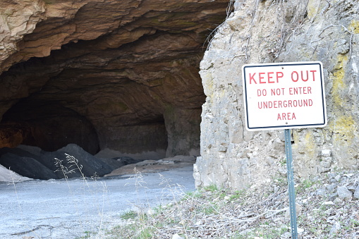 Keep out sign by the entrance to an underground cave.  Keep out sign is prominent and background shows a dark cave.