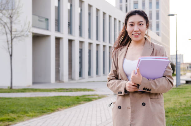 istock Asian university student looking at the camera and holding folders while standing outdoors at the college campus 1310735905