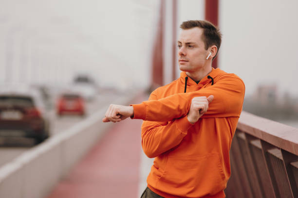 hombre corredor estira los brazos en un puente - orange white audio fotografías e imágenes de stock