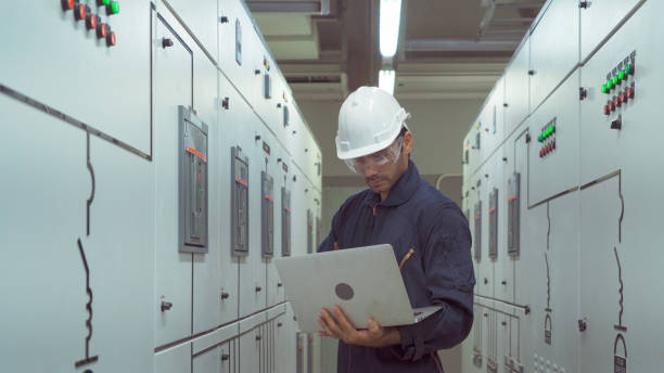 um engenheiro ou trabalhador, pessoas usando um computador portátil, trabalhando em sala elétrica. gabinetes de máquinas de motores de energia elétrica em sala de controle ou servidor, rede de estações de operadores na fábrica do setor. - fornecimento de energia - fotografias e filmes do acervo