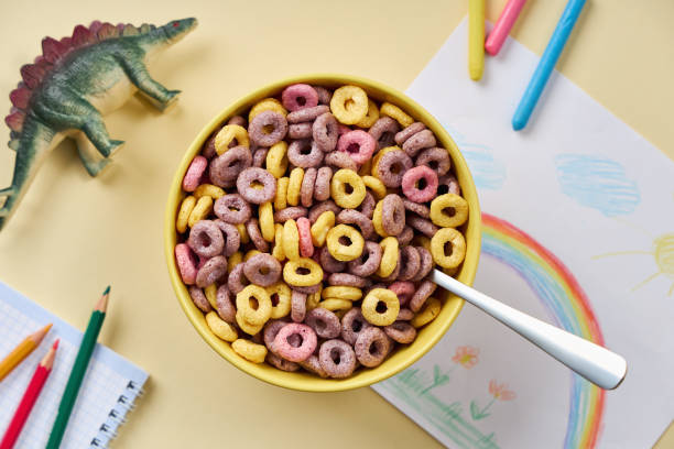 Top view of multi-colored cornflakes in a bowl on the background of children`s drawing and toys.