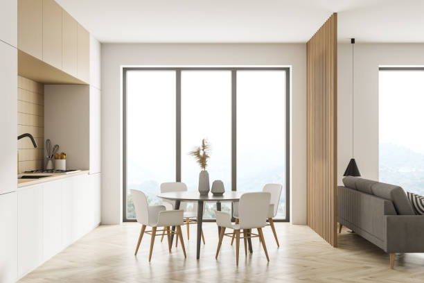 istock Modern kitchen interior, dining area and living room space with panoramic windows with countryside and hills view. Furnished by table and chairs for eating, beige sofa. 1310746304