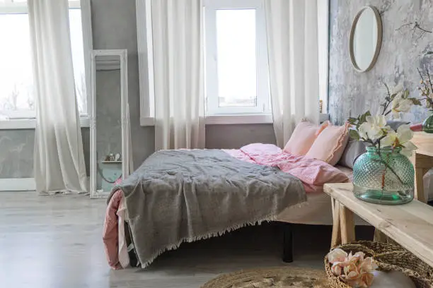 Side view on a bedroom bed with grey and pink bedding, white mirror and vases with flowers