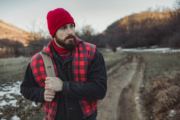 istock Lumberjack, attractive looking. A bearded man walks through the woods while the sunset is behind him. A man, a lumberjack, goes to his log cabin, which is in a deep forest. 1310747489