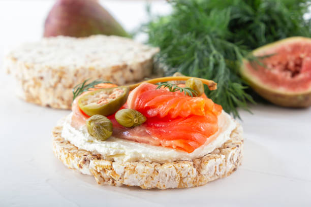 istock Puffed exploded wheat grains with a slice of red fish, olives and capers on a thin layer of soft cheese on a light wooden table against a background of greens. 1310748732