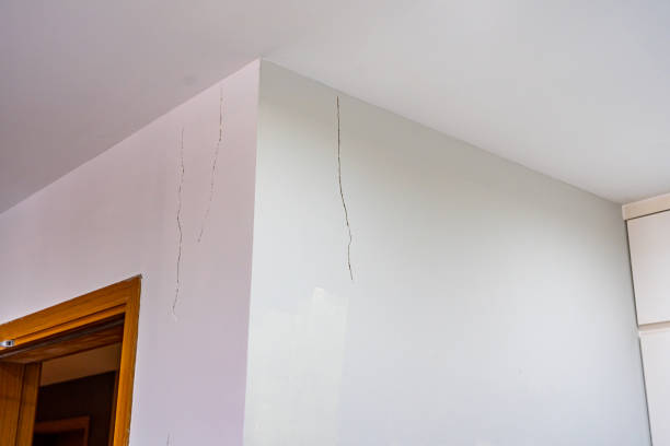 White painted wall with cracks near the ceiling stock photo