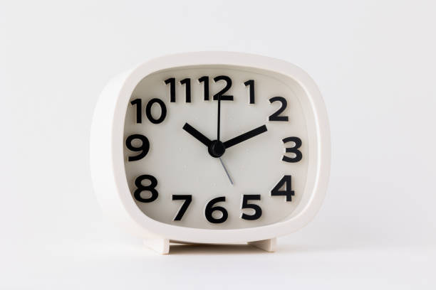 istock Small white alarm clock, black numbers, set the time for 10.10 o'clock, placed on a white table. 1310754859