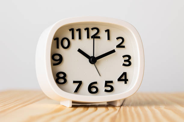 istock Small white alarm clock, black numbers, set the time for 10.10 o'clock, placed on a wood table. 1310754873