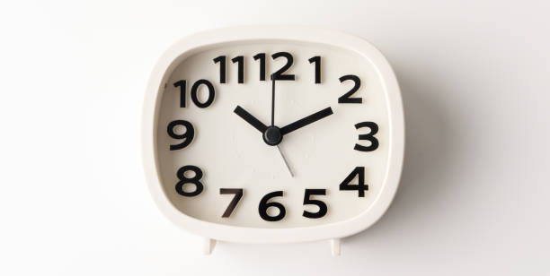 istock Small white alarm clock, black numbers, set the time for 10.10 o'clock, placed on a white table. 1310754880