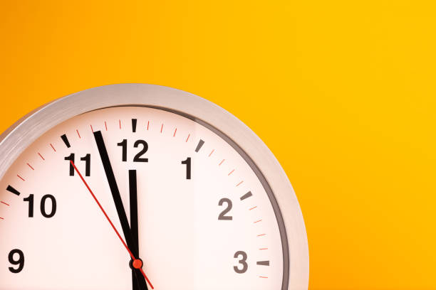 istock Large white alarm clock, black numbers, set the time placed on a table. Clock on isolated yellow background. 1310754881
