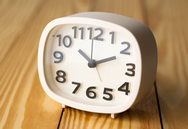 istock Small white alarm clock, black numbers, set the time for 10.10 o'clock, placed on a wood table. 1310754886