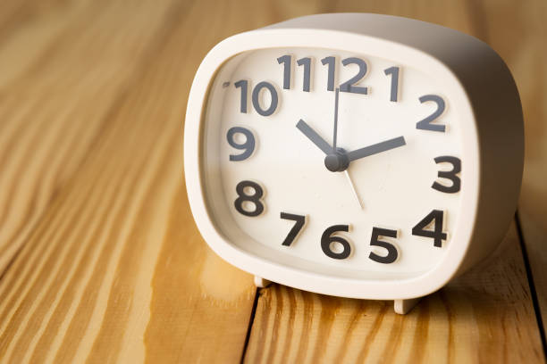 istock Small white alarm clock, black numbers, set the time for 10.10 o'clock, placed on a wood table. 1310754898