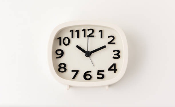 istock Small white alarm clock, black numbers, set the time for 10.10 o'clock, placed on a white table. 1310754907