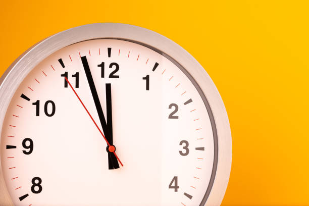 istock Large white alarm clock, black numbers, set the time placed on a table. Clock on isolated yellow background. 1310754909