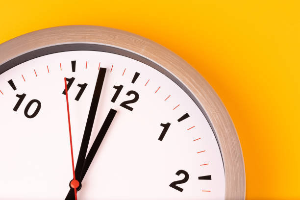 istock Large white alarm clock, black numbers, set the time placed on a table. Clock on isolated yellow background. 1310755420