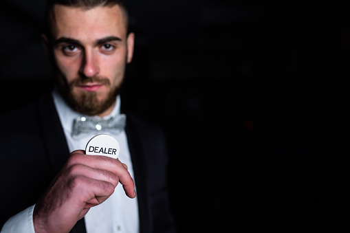 A handsome young man in a suit is holding the dealer button between his fingers