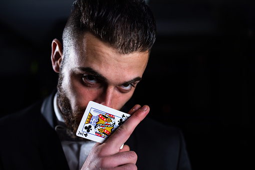 A handsome man in a suit is hiding the lower half of his face behind the king of clubs card