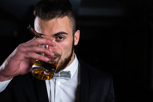 Pouring whiskey from a bottle into glass with ice standing on a dark table on a black background