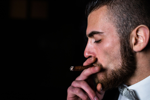 A handsome man in a suit is smoking a cigar in the dark