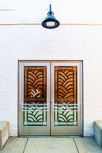 Exterior Art Deco glass and metal doors in white brick wall. Light fixture above doors.