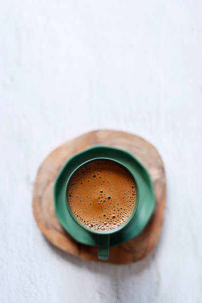 ahşap bardak altlığında açık gri beton zeminde yeşil seramik bardakta köpüklü türk kahvesi, yakın çekim - türk kahvesi stok fotoğraflar ve resimler