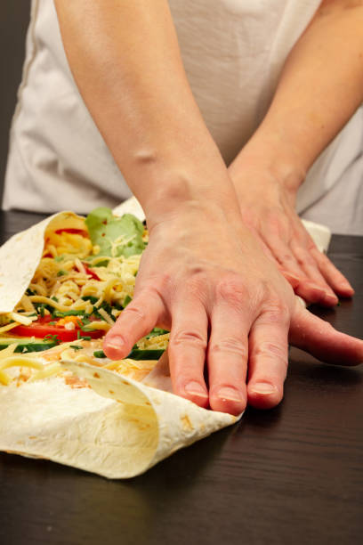 female hands wrap fresh vegetable salad with cheese in pita bread. cooking shawarma on a wooden table